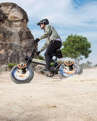 Person riding a balance OTIDA R7 MAX Dual Motor Electric Bike with large wheels on a rocky path