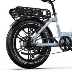 Close-up rear view of a light blue onesport OT08 electric bicycle with a black rear cargo basket, black fender, fat tire, disc brakes, and chainring, on a white studio background.
