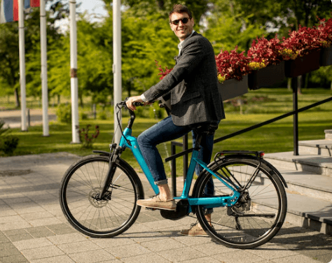 Smiling man riding blue electric bike outdoors, promoting Pogo Cycles e-bike collection