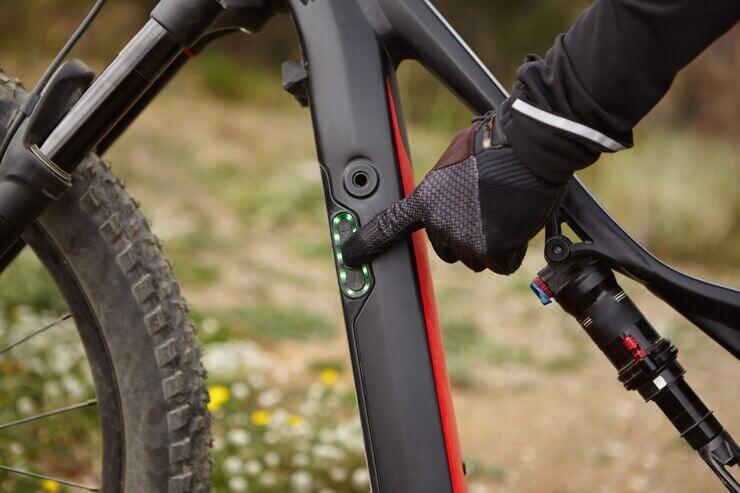 Close-up of gloved hand pressing battery indicator on electric mountain bike at Pogo Cycles