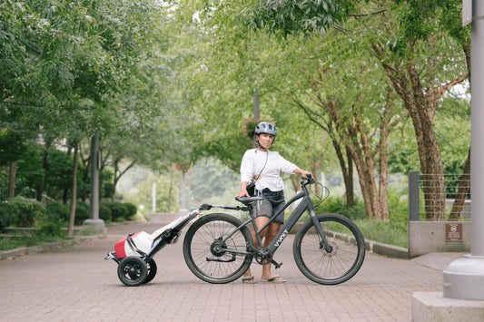 Woman with electric bike and cargo trailer on tree-lined park path, Pogo Cycles e-bike
