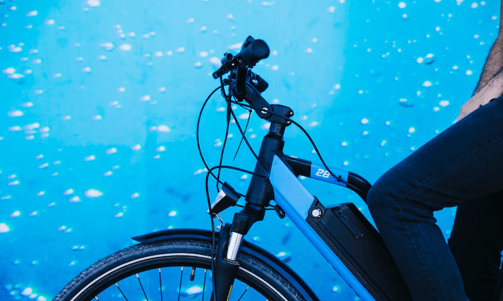 Close-up of person riding electric bike against blue background, Pogo Cycles e-bike store