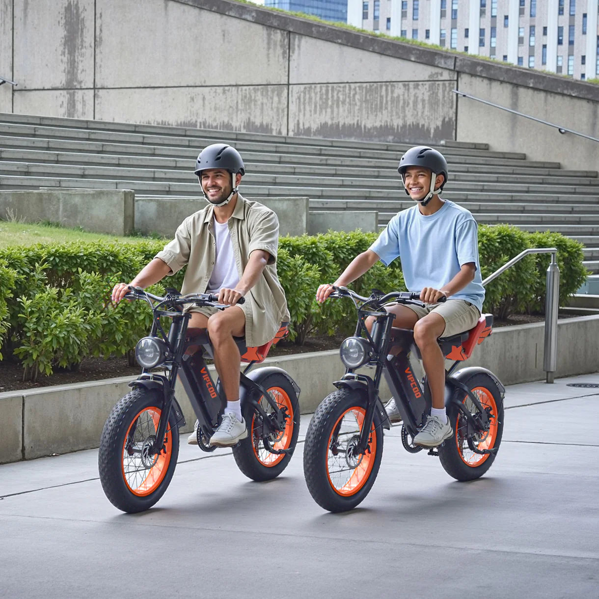 Two people riding VIPCOO VM6 Electric City Bikes on a city street with buildings in the background
